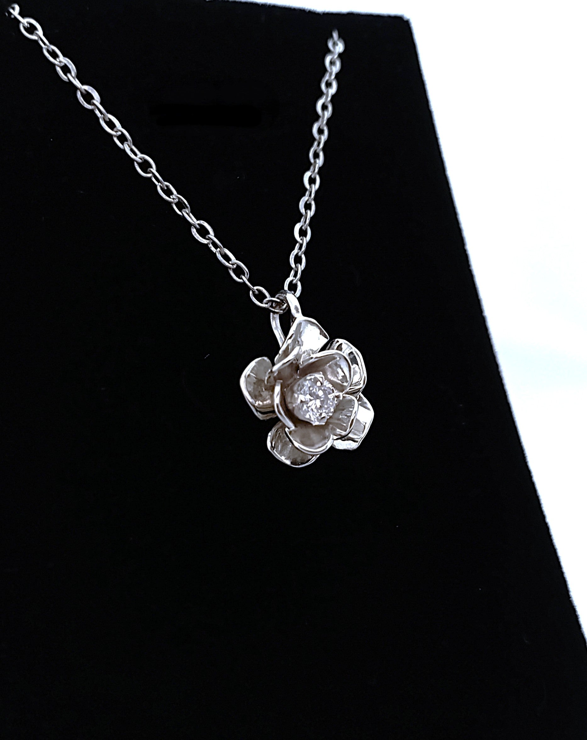 Silver necklace with a flower-shaped pendant on a black background