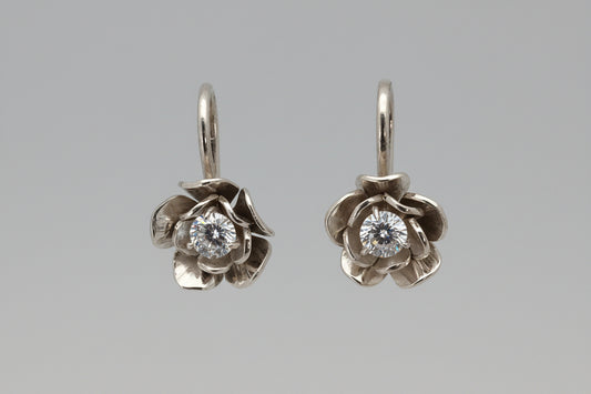 Flower-shaped silver earrings with clear gemstones on a black background