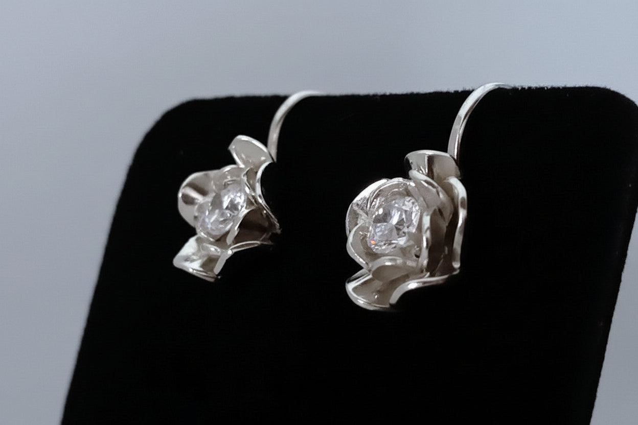 Pair of silver earrings with clear gemstones on a black stand.