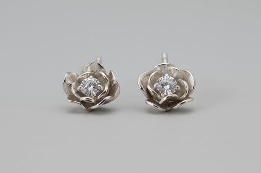 Pair of silver flower-shaped earrings with clear gemstones on a black background