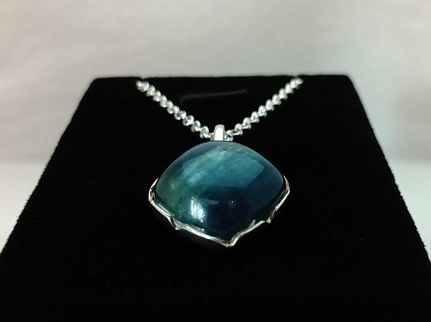 Blue pendant necklace on a black stand with a white background