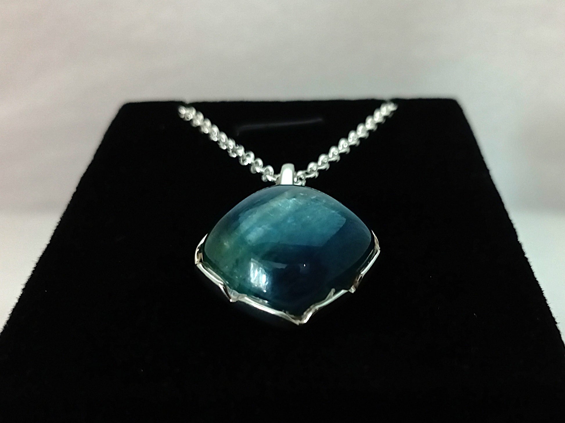 Blue pendant necklace on a black stand with a white background